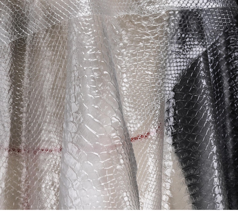 May include: Close-up of a clear, textured plastic sheet with a crocodile skin pattern. The sheet is translucent and has a slight sheen.
