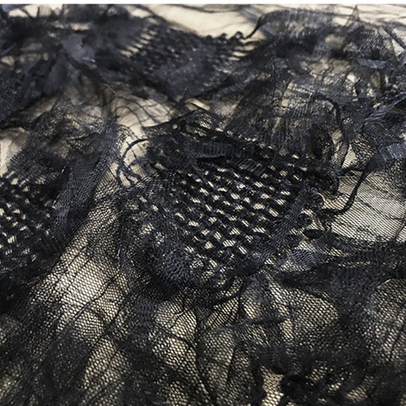 May include: Black lace fabric with a delicate floral pattern. The fabric is sheer and has a soft, flowing texture.