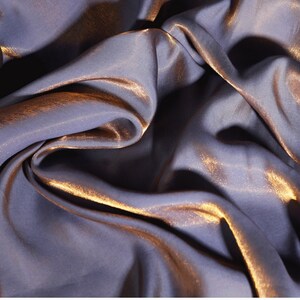 May include: A close-up of a soft, silky fabric with a metallic sheen. The fabric is a deep purple color with a subtle gold shimmer.