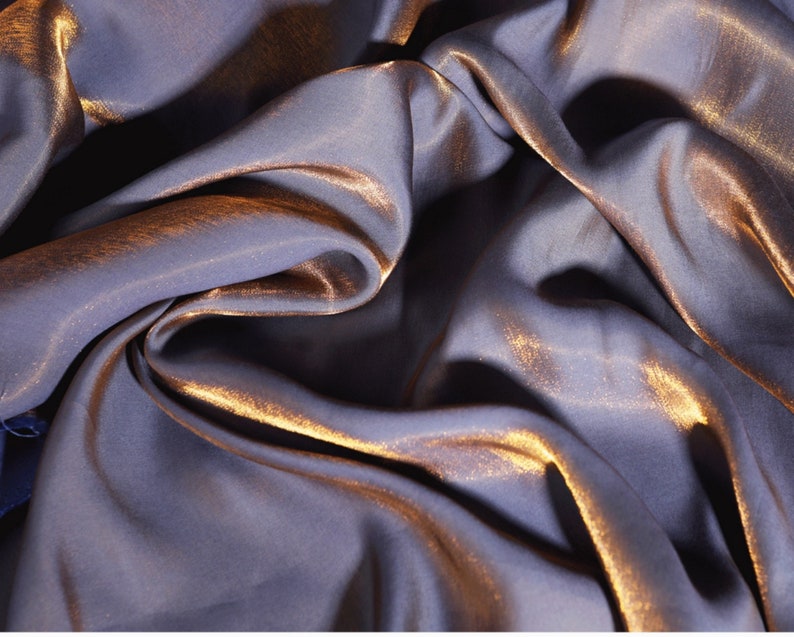 May include: A close-up of a soft, silky fabric with a metallic sheen. The fabric is a deep purple color with a subtle gold shimmer.