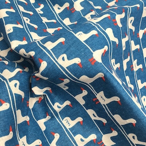 May include: White geese with red beaks are printed on a blue fabric with white stripes. The fabric is folded and textured.