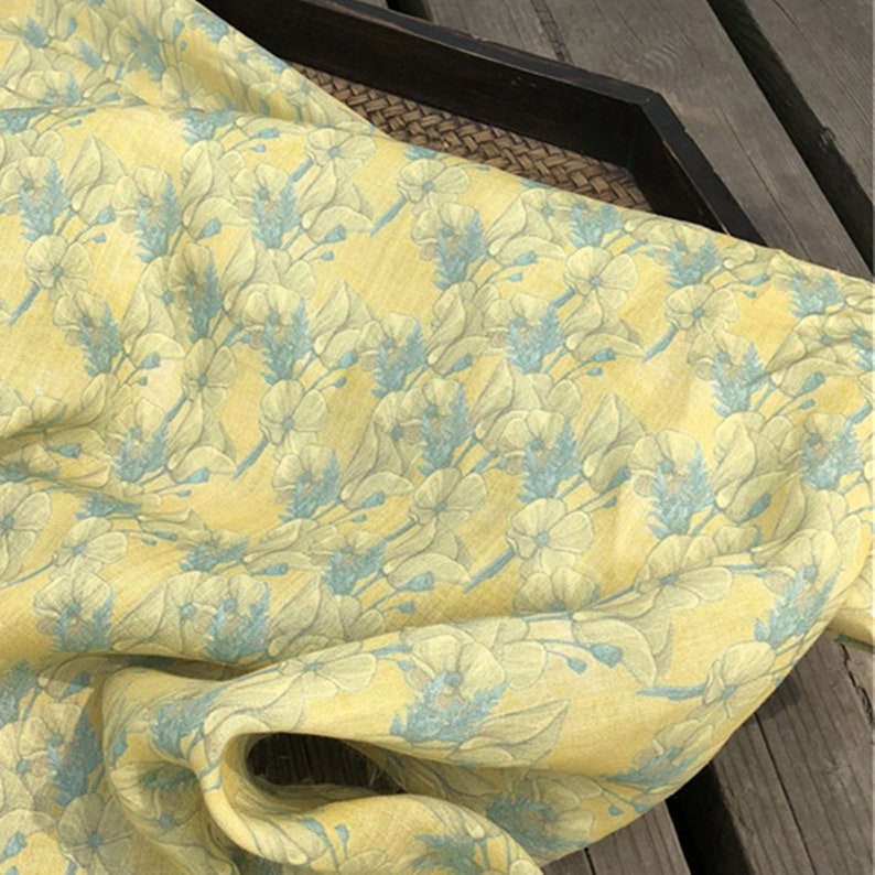 May include: Yellow linen fabric with a blue floral pattern. The fabric has a textured, woven look.