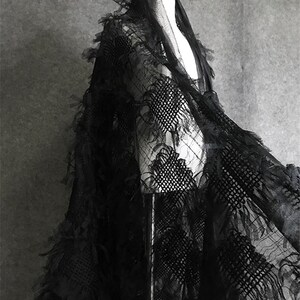 May include: Black lace fabric with a textured, fringed design. The fabric is draped over a mannequin.