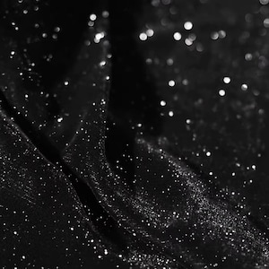May include: Black fabric with a sparkly, glittery texture. The fabric is draped and folded, creating a soft, flowing look.
