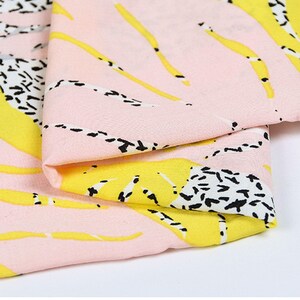 Op de afbeelding: Roze stof met een abstracte print in geel en zwart. De stof is dubbelgevouwen, waardoor het patroon aan beide kanten zichtbaar is.