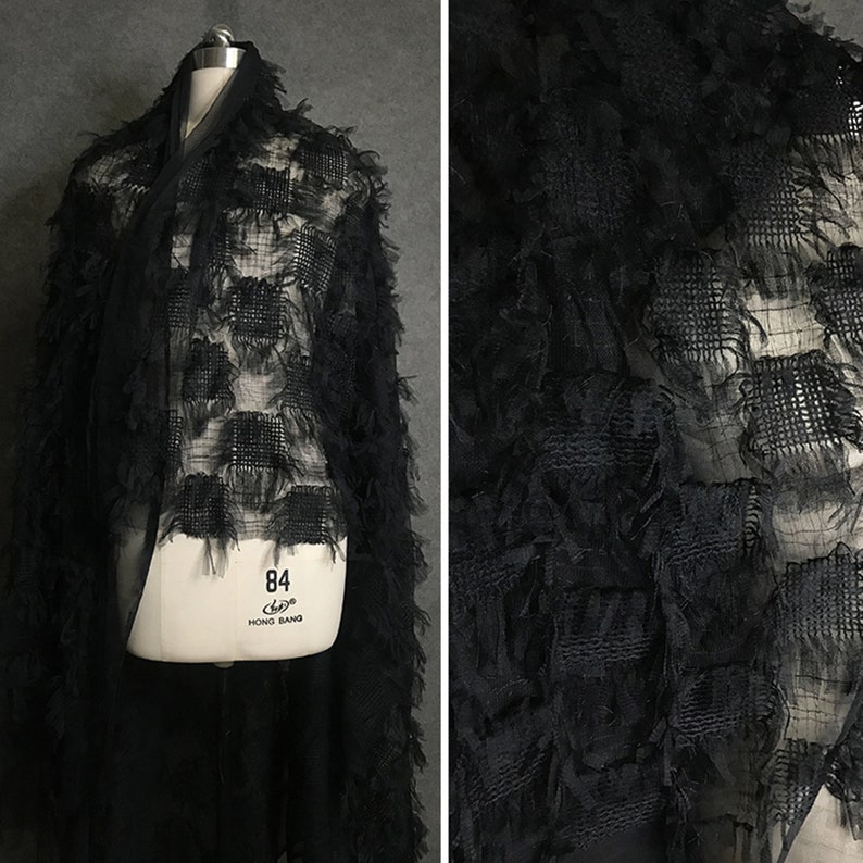 May include: Black sheer fabric with a textured, fringed design. The fabric has a grid pattern with square-shaped fringes.