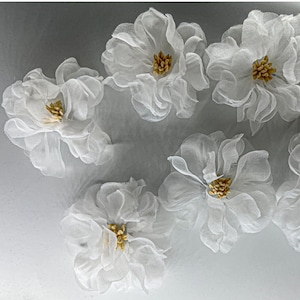 May include: Five white fabric flowers with gold centers. The flowers are arranged in a semi-circle on a gray background.