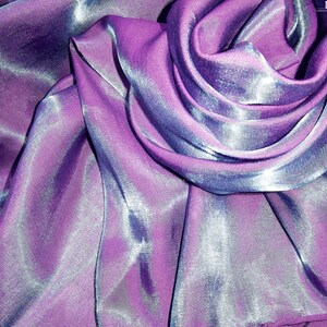 May include: Close-up of a shimmering purple and blue fabric with a silky texture. The fabric is draped and folded, creating soft curves and folds.