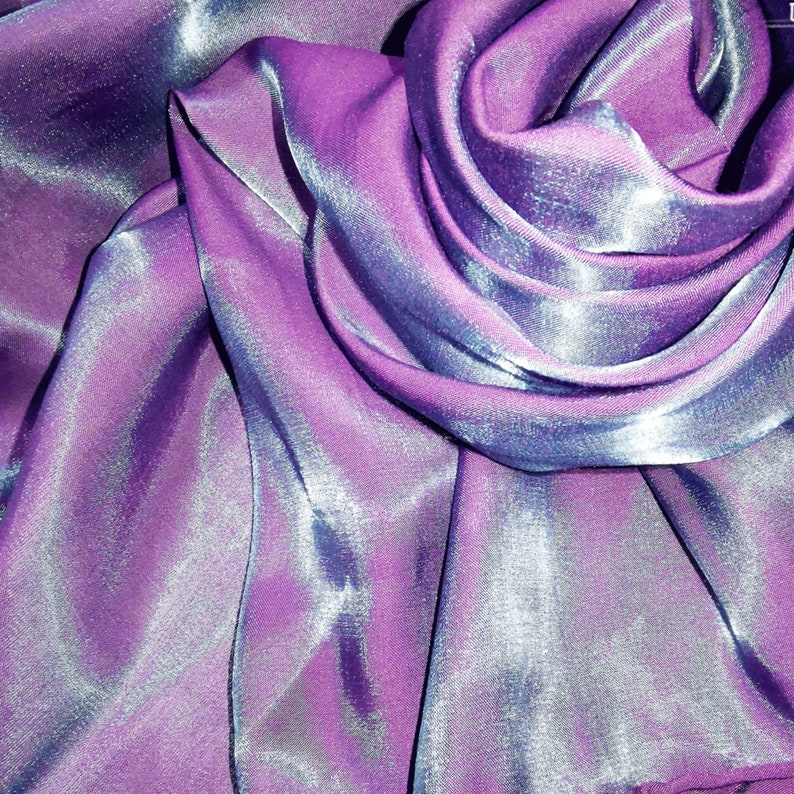 May include: Close-up of a shimmering purple and blue fabric with a silky texture. The fabric is draped and folded, creating soft curves and folds.