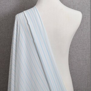May include: White fabric with thin blue stripes. The fabric is draped over a white dress form.