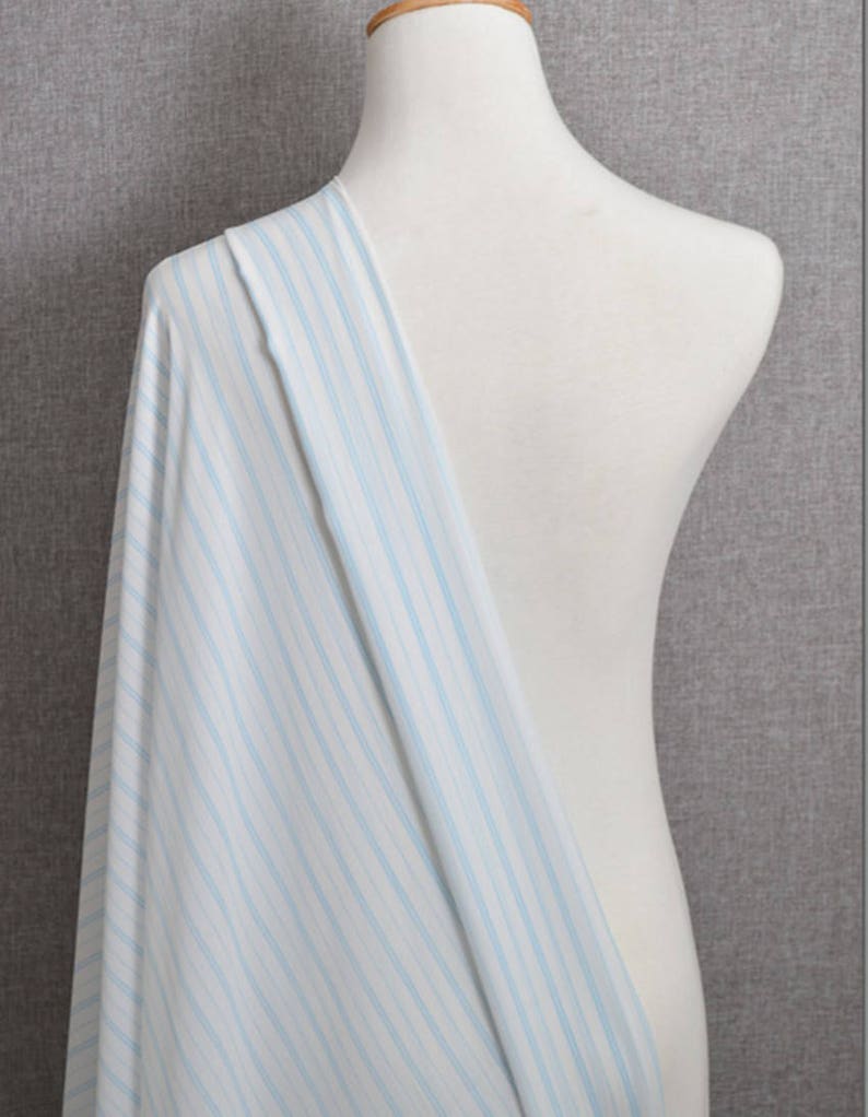 May include: White fabric with thin blue stripes. The fabric is draped over a white dress form.