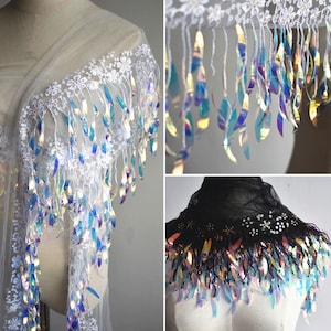 Pode incluir: Tecido de renda branca com acabamento de franjas iridescentes. A franja é feita de pequenas lantejoulas iridescentes que brilham à luz. O tecido é transparente e delicado, e seria perfeito para uma variedade de projetos, como roupas, acessórios e decoração de casa.
