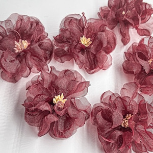 May include: Six burgundy-colored fabric flowers with a ruffled texture. The flowers have a light yellow center.