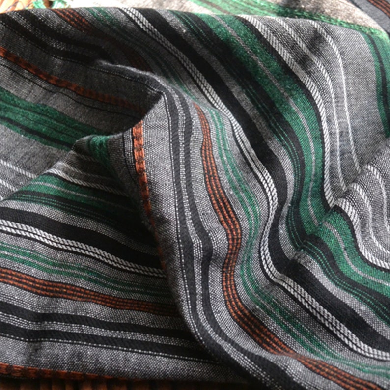 May include: Close-up of a fabric with black, white, green, and orange stripes. The fabric is woven and has a textured surface.