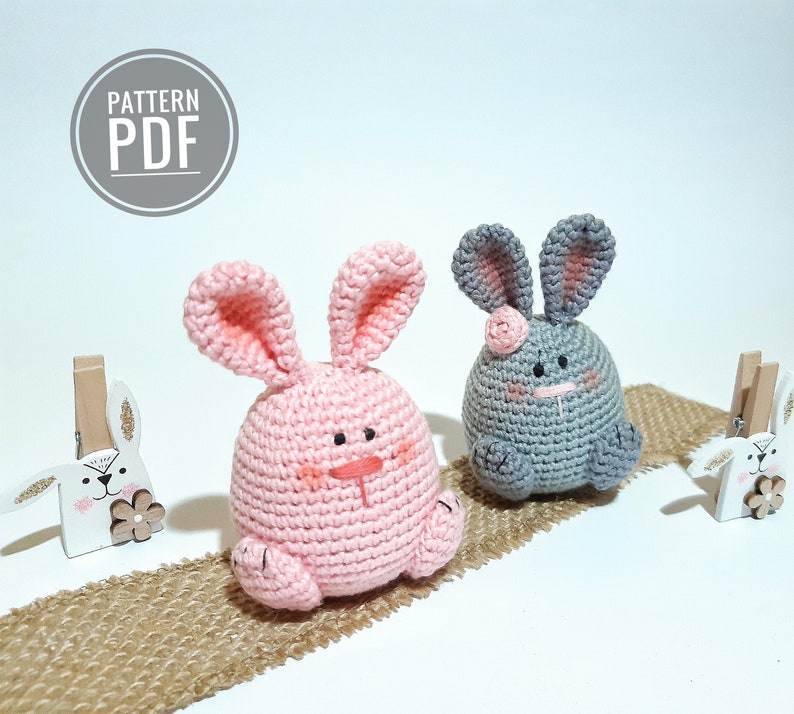 May include: Two crocheted bunny amigurumi toys, one pink and one gray, with embroidered facial features. The bunnies are sitting on a burlap surface. The text "PATTERN PDF" is visible in the top left corner of the image.