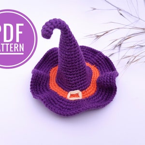 Könnte beinhalten: Ein lilafarbener Häkelhut mit orangefarbenem Band und Schnalle. Der Hut liegt auf einer weißen Oberfläche.
