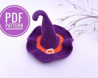 Könnte beinhalten: Ein lilafarbener Häkelhut mit orangefarbenem Band und Schnalle. Der Hut liegt auf einer weißen Oberfläche.