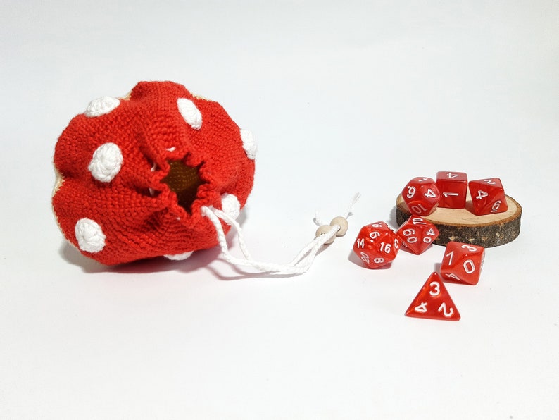 Pode incluir: Uma bolsa de dados de croch&ecirc; vermelha com bolinhas brancas e um cord&atilde;o de ajuste. A bolsa est&aacute; aberta e os dados vermelhos com n&uacute;meros brancos est&atilde;o caindo.