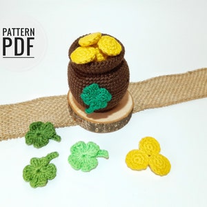 May include: A brown crocheted pot filled with yellow crocheted coins, sitting on a wooden base.  Four green crocheted shamrocks and one yellow crocheted shamrock are scattered around the pot.  The text "PATTERN PDF" is in white on a black circle.