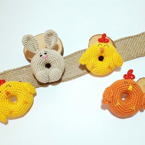 May include: Three crocheted stuffed animals: a bunny, a yellow chick, and an orange chick. The bunny is beige and has a pink nose. The chicks have red beaks and feet. All three animals are shaped like donuts.