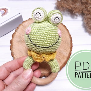 May include: Crochet frog rattle with a wooden ring. The frog is green with pink cheeks and black eyes. The rattle is a great toy for babies and toddlers.
