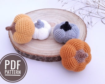 Könnte beinhalten: Vier gehäkelte Kürbisse in verschiedenen Farben, darunter Orange, Weiß, Grau und Braun, auf einer Holzscheibe. Die Kürbisse sind alle etwa 7,5 cm hoch. Das Bild enthält auch den Text "PDF PATTERN".