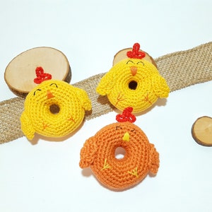 May include: Three crocheted chick toys in the shape of donuts. The chicks are yellow and orange with red beaks and feet.