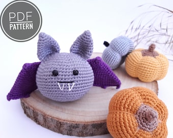May include: Crocheted Halloween decorations including a purple and gray bat with fangs, a gray pumpkin, and two orange pumpkins.