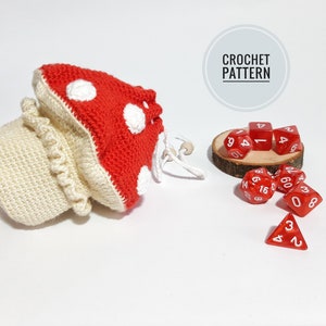 May include: Crochet mushroom dice bag with red and white yarn, and red dice with white numbers. The bag is sitting on a white surface. CROCHET PATTERN is written on a gray circle.