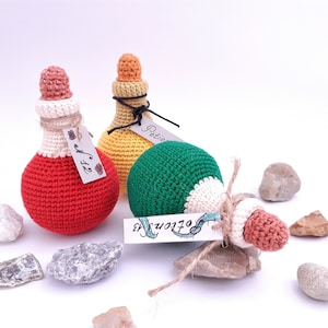 Puede incluir: Tres botellas de poci&oacute;n de crochet con tapones de corcho y etiquetas. Las botellas son roja, amarilla y verde. Las etiquetas dicen "Poci&oacute;n", "Tama&ntilde;o" y "Pociones".