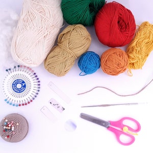 Puede incluir: Una colecci&oacute;n de hilo de varios colores, incluyendo blanco, verde, rojo, amarillo, naranja y azul, junto con un coj&iacute;n de alfileres, un gancho de ganchillo, unas tijeras y una peque&ntilde;a etiqueta.