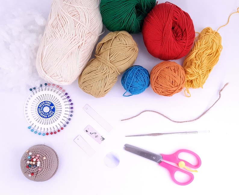 Puede incluir: Una colecci&oacute;n de hilo de varios colores, incluyendo blanco, verde, rojo, amarillo, naranja y azul, junto con un coj&iacute;n de alfileres, un gancho de ganchillo, unas tijeras y una peque&ntilde;a etiqueta.