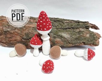 Può includere: Cinque funghi all'uncinetto, tre con cappelli rossi e bianchi e due con cappelli marroni. I funghi sono disposti su una superficie bianca con un pezzo di corteccia d'albero dietro di loro. Il testo "PATTERN PDF" è visibile in un cerchio sulla corteccia.