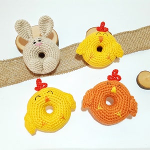 May include: Four crocheted stuffed animals: a bunny and three chicks. The bunny is beige and the chicks are yellow and orange. The chicks have red beaks and feet. The animals are all shaped like donuts.