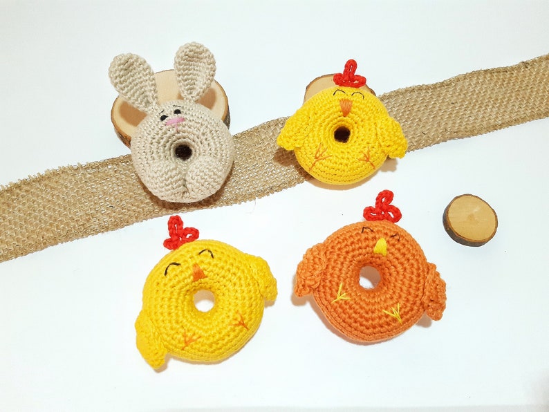 May include: Four crocheted stuffed animals: a bunny and three chicks. The bunny is beige and the chicks are yellow and orange. The chicks have red beaks and feet. The animals are all shaped like donuts.