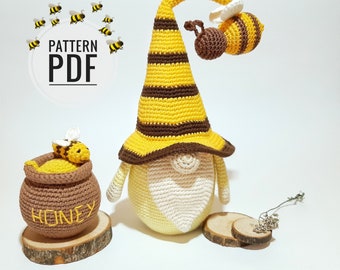 May include: A crocheted gnome with a yellow and brown striped hat, holding a honey pot with a crocheted bee on top. The gnome is standing on a wooden base. The text "PATTERN PDF" is visible in the background.