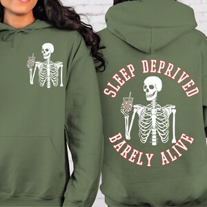 May include: Green hooded sweatshirt with a white skeleton holding a cup of coffee on the front and a white skeleton holding a cup of coffee with the text "SLEEP DEPRIVED BARELY ALIVE" on the back.