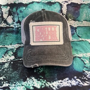 May include: A black and gray distressed trucker hat with a pink patch that says "Pretty Rogue Soul".