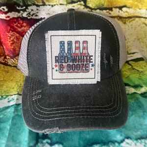 May include: A black and gray distressed trucker hat with a white patch that says "Red White & Booze" with a graphic of three beer bottles with American flag designs.