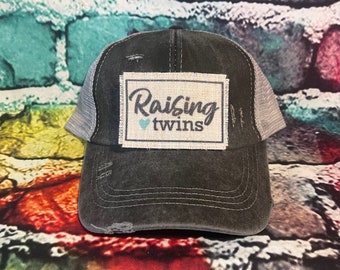 May include: A black and gray distressed trucker hat with a patch that says "Raising twins" with a small blue heart.