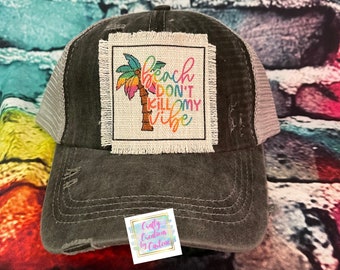 May include: A distressed charcoal gray trucker hat with a white mesh back. The front patch features a colorful palm tree and the text "Beach Don't Kill My Vibe." The hat has a curved brim and a small tag with text.