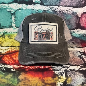 May include: A black and gray distressed trucker hat with a white patch that says "Beautiful Crazy" in black lettering. The patch is made of fabric and has a vintage look.