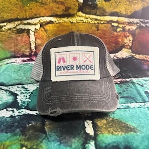 May include: A black and gray distressed trucker hat with a tan patch that says "River Mode Activated" with a tent, sun, and crossed paddles graphic.