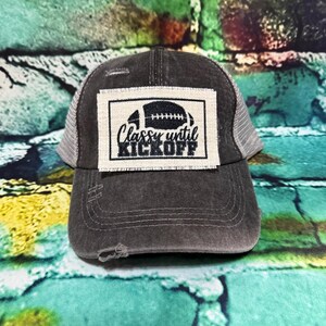 May include: A distressed charcoal gray trucker hat with a white and black patch featuring a football graphic and the text "Classy until Kickoff." The hat has a mesh back and a curved brim, perfect for game day.