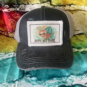 May include: Black and gray distressed trucker hat with a white patch featuring a cartoon sloth and the text "NOPE. NOT TODAY."
