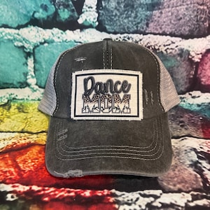 May include: A black and gray distressed trucker hat with a white patch that says "Dance Mom" in black with a leopard print design.