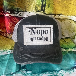 May include: A black and gray trucker hat with a distressed look. The hat has a white patch with the text "Nope not today" in black.