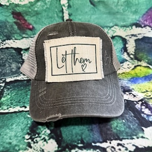 May include: A black and gray distressed trucker hat with a white patch that says "Let them ♥".