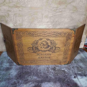 Op de afbeelding: Een houten Dungeon Master-scherm met een Keltische knooprand en een grafische weergave van een 20-zijdige dobbelsteen. Het scherm heeft drie panelen en staat in het midden "Dungeon Master".