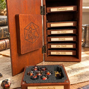 May include: A wooden storage case with a hinged door featuring an engraved dragon and d20 design. The interior contains multiple shelves with labels including Darkstep, Sir Dare, Arioch, The Bard, and The DM. A removable tray holds dice.